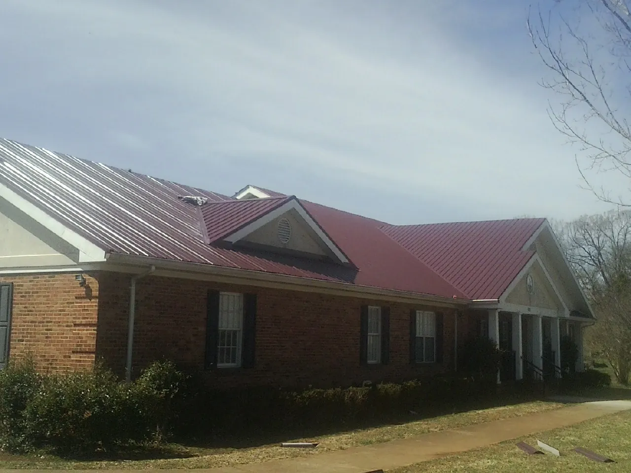 Red metal roof with gabled entries on a long brick building, from a Hail Damage Roof Repair job in South Bay