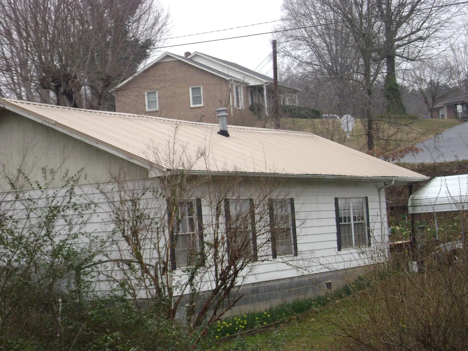 Tan metal roof on a white sided house set into a hillside — Commercial Roofing by Roofing Brothers in South Bay